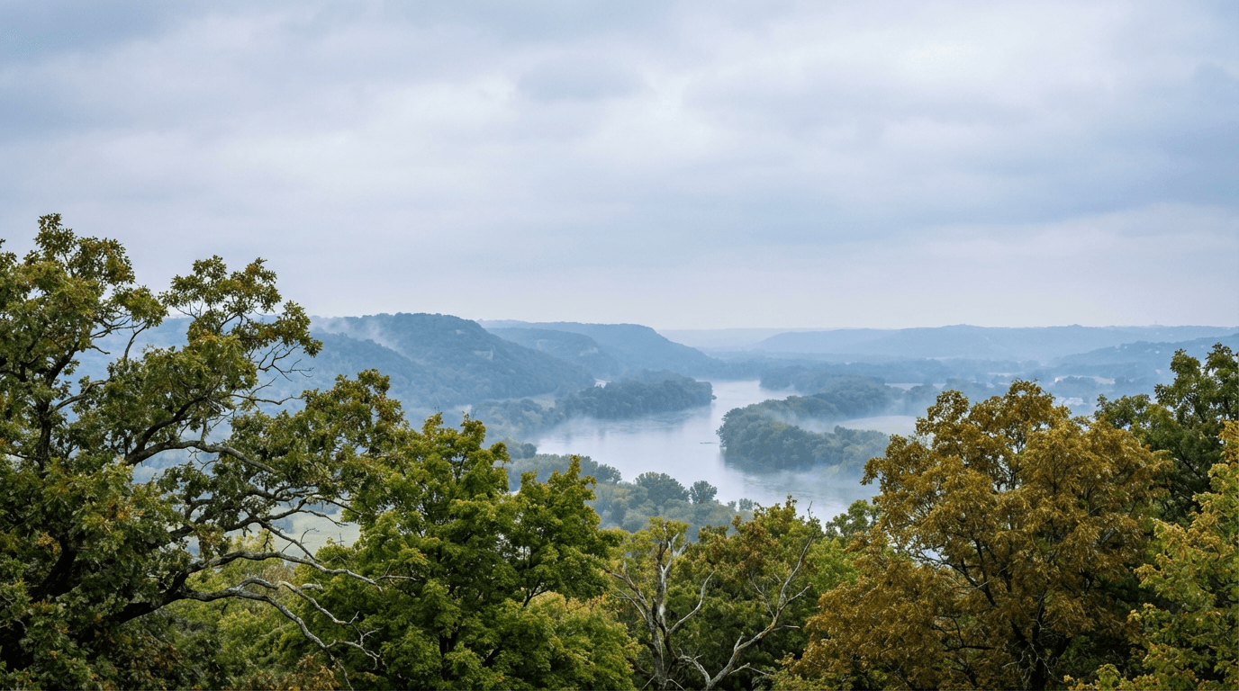 Rolling Missouri River valley landscape near Independence with drone advancing through misty tree layers toward distant bluffs.
