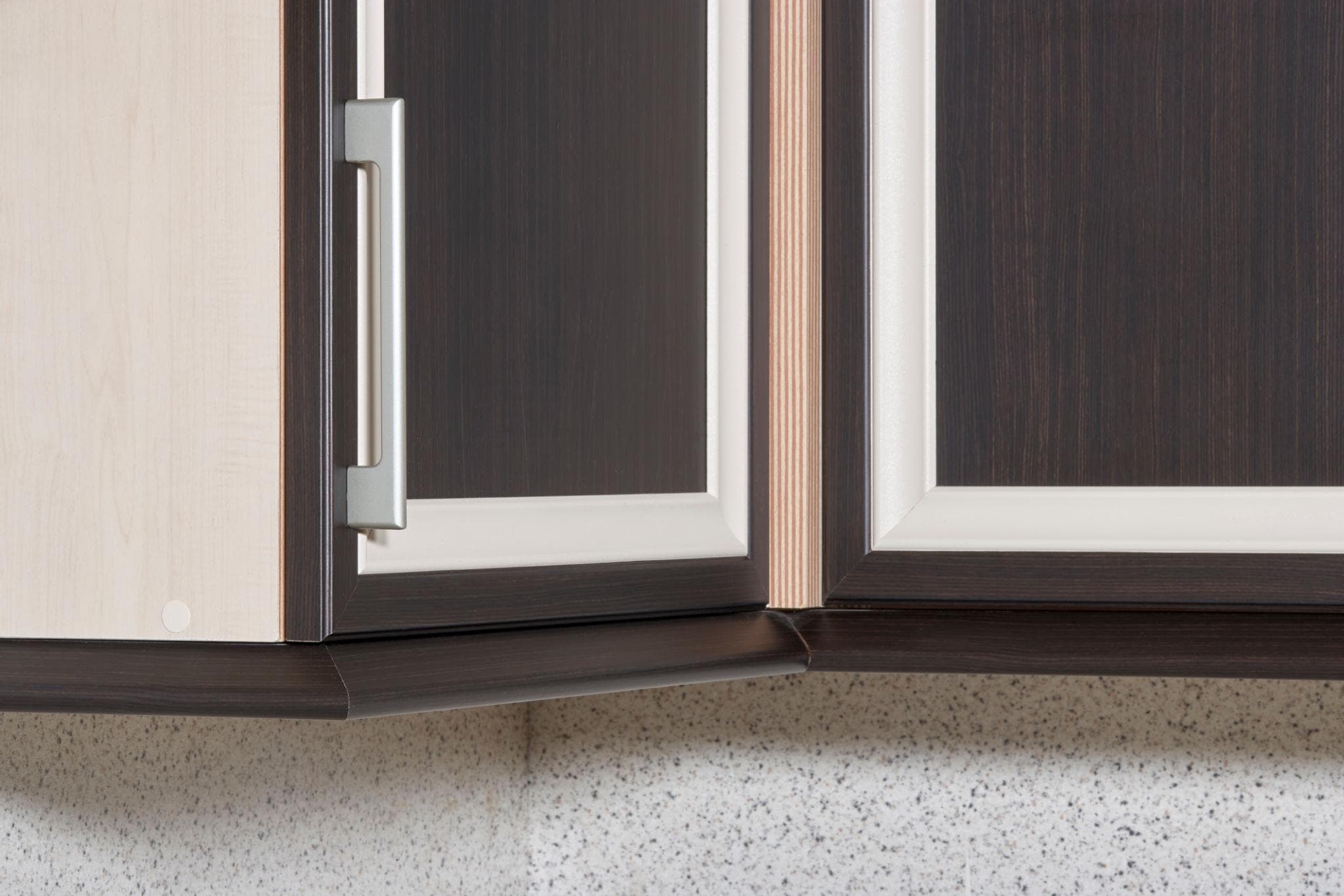 Dark wood kitchen cabinets with cream trim and a silver handle over a speckled backsplash.