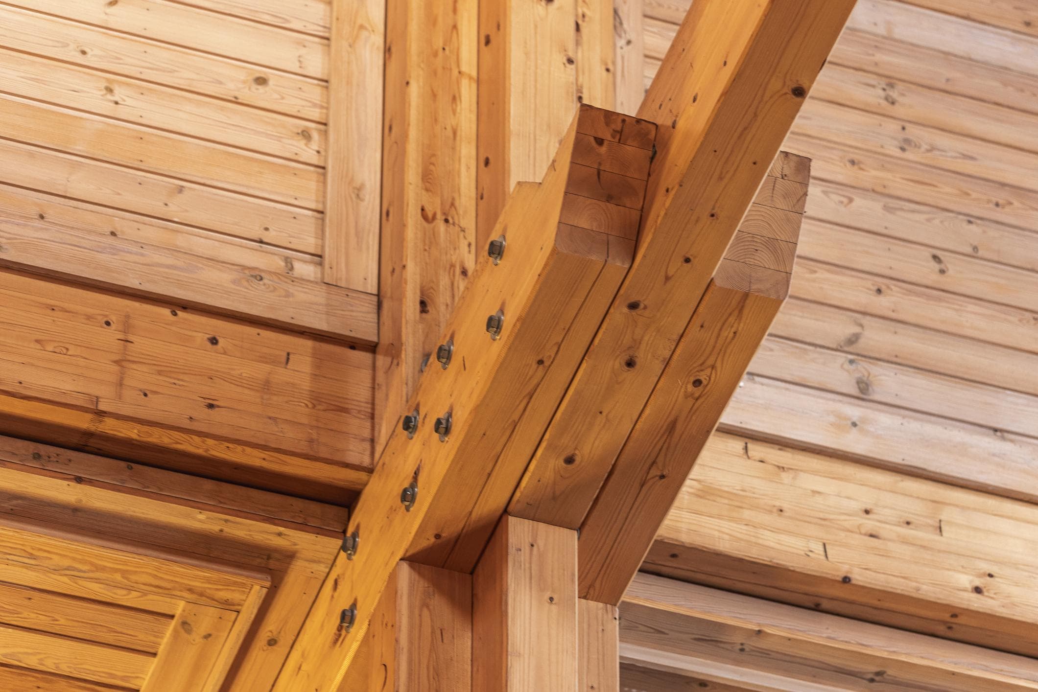 Heavy timber beams and structural joints fastened with metal bolts in a wooden building.