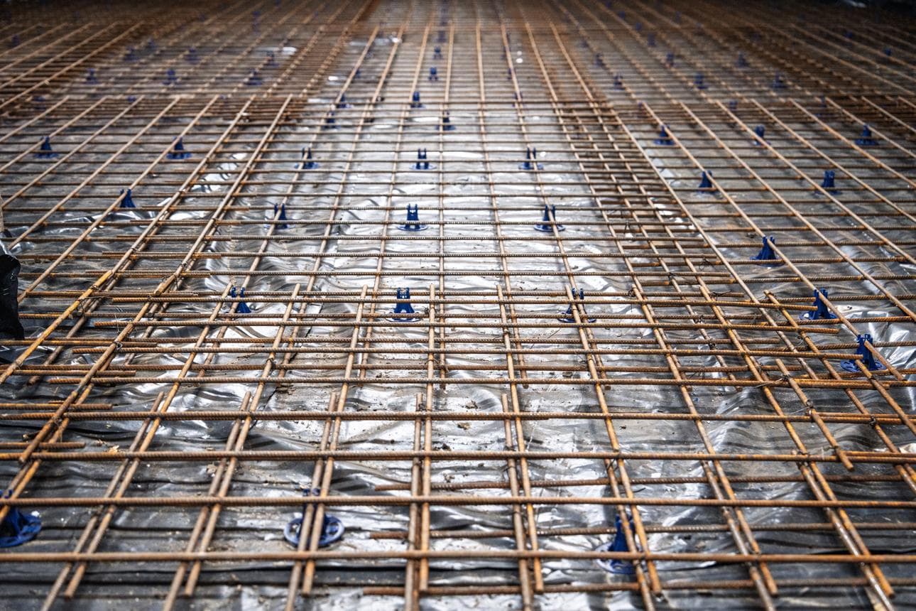 Steel rebar grid supported by blue plastic spacers over a silver moisture barrier for construction.