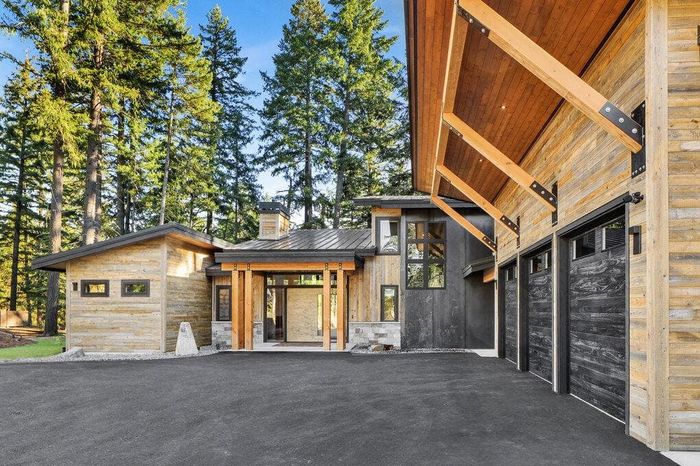 Modern home with wood siding, black metal accents, and large windows, nestled in a forest.