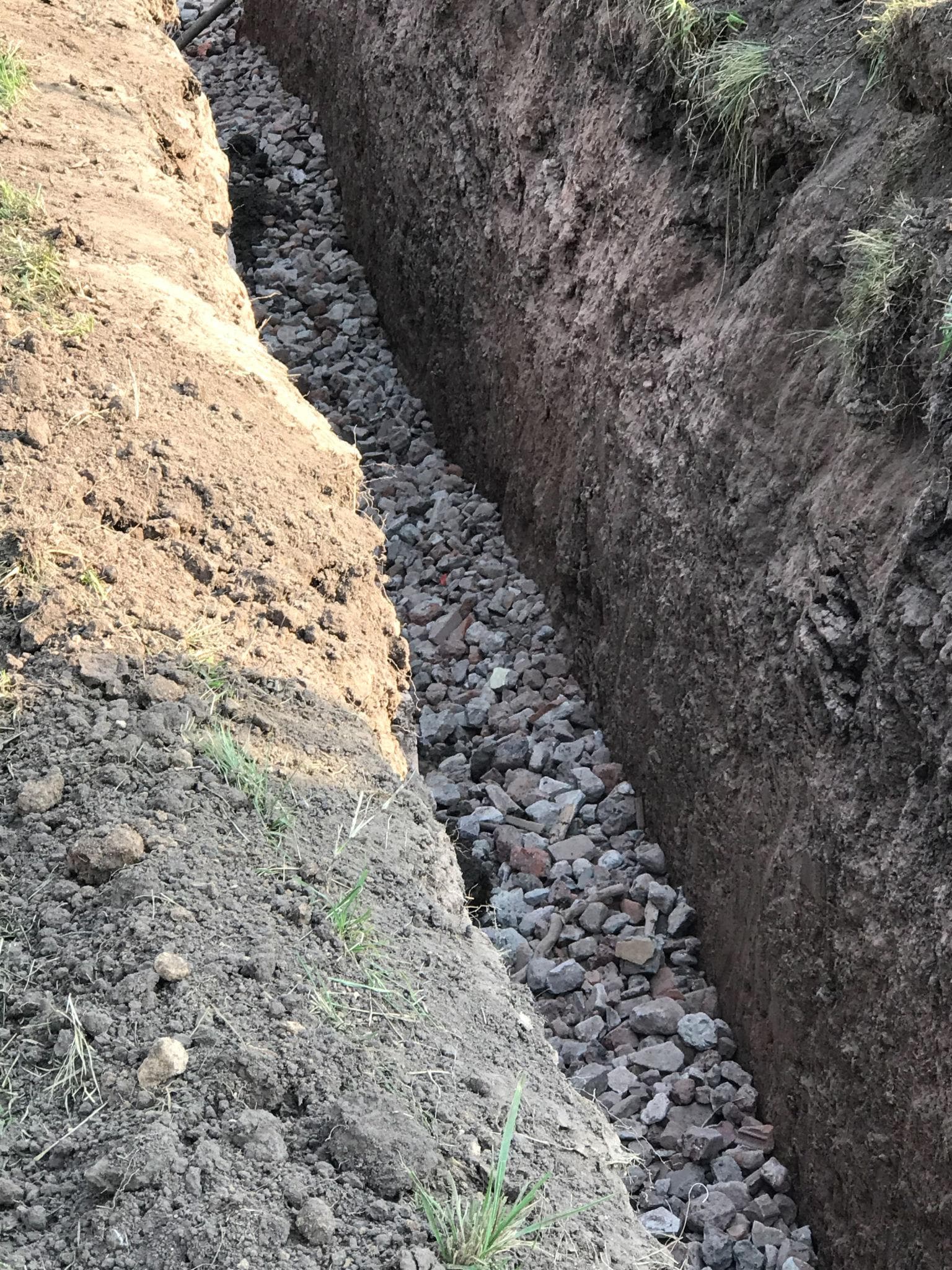 Deep earthen trench with vertical walls and a bottom layer of grey crushed stone gravel.